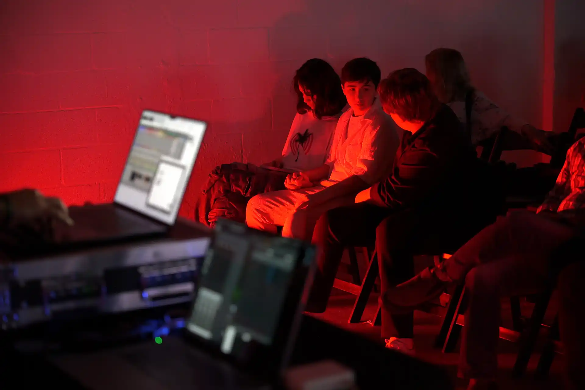 People talking and using laptops in a dimly lit space with red ambient lighting.