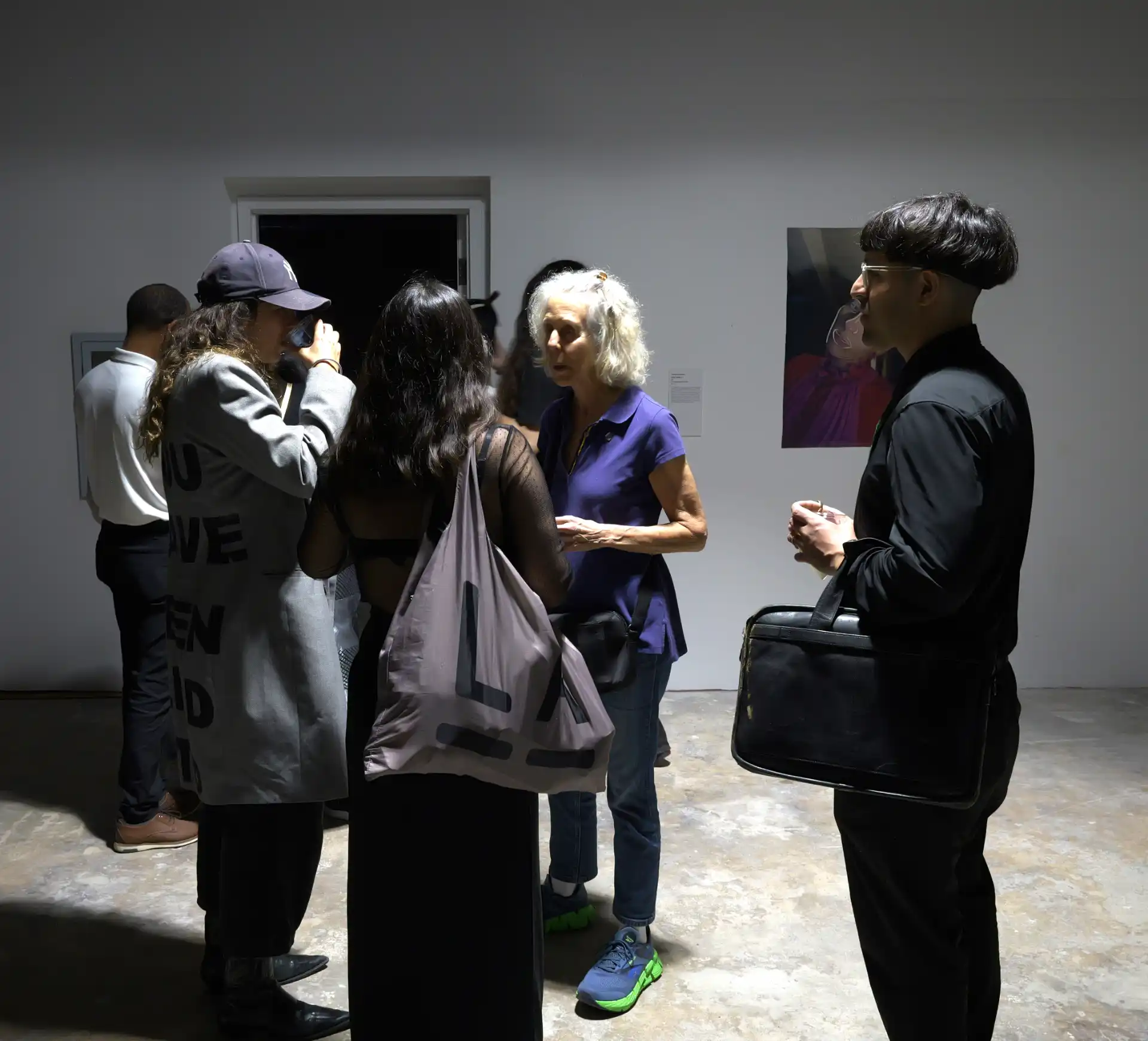 Group of people conversing and drinking at an art gallery with a painting on the wall.