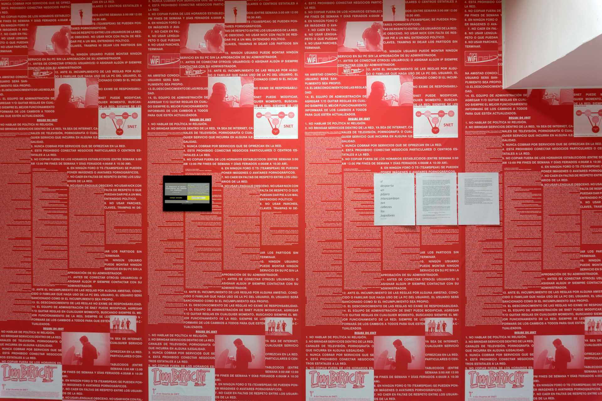 A wall with red paper wall with messages of a poem by Ernesto Oroza for SNET called Si despierta un p&aacute;jaro intercambian sus cabezas los jugadores